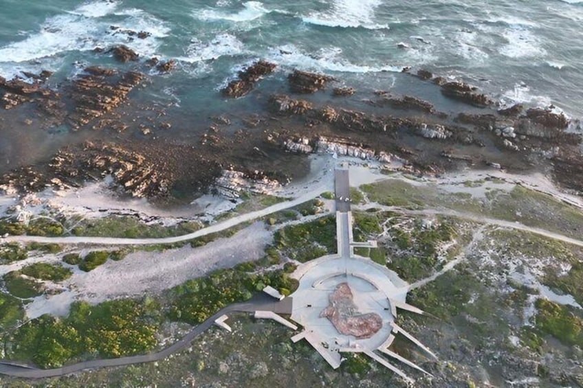 A coastal area with rocky shores, a circular monument, and a winding path. 1