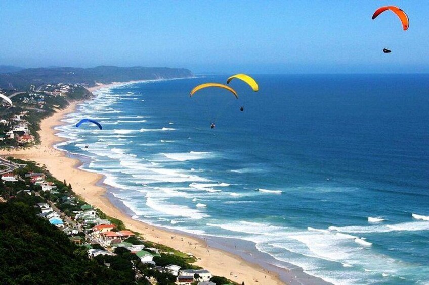 A beach with people paragliding, waves, and coastal buildings. 5