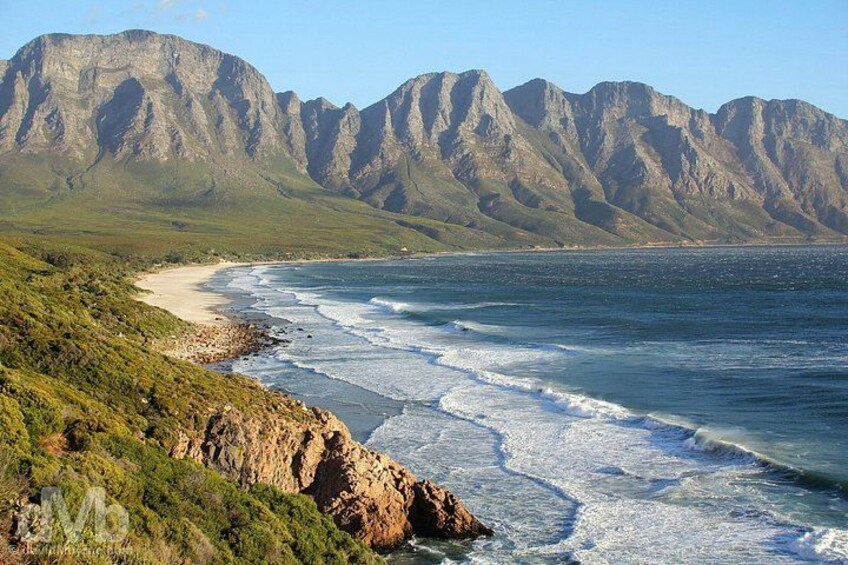 A coastal landscape with a beach, rocky cliffs, and mountains in the background. 3
