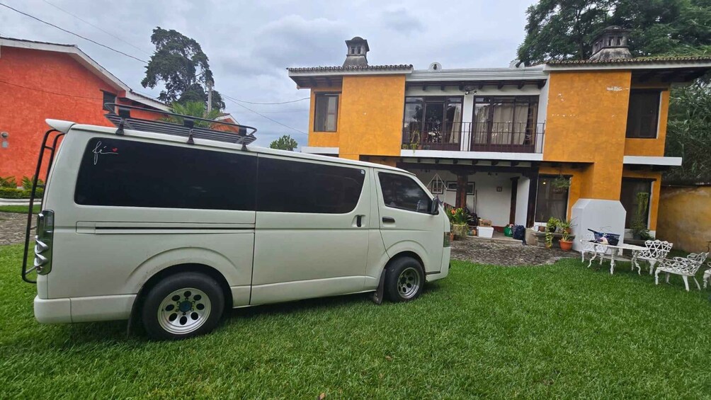A white van parked on a lawn in front of a yellow building with a balcony. 2