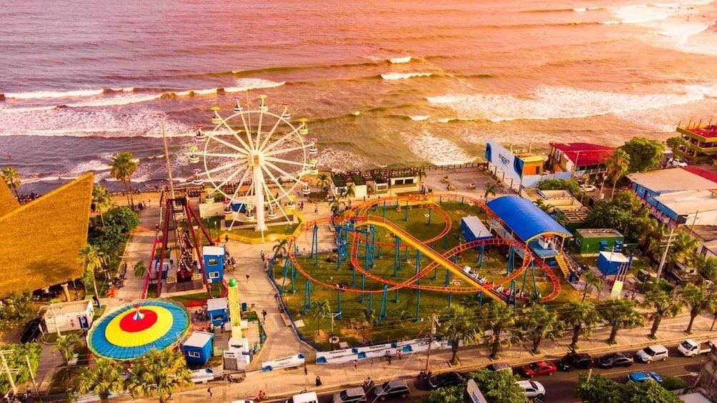 A coastal amusement park with a Ferris wheel, roller coasters, and a water slide. 3