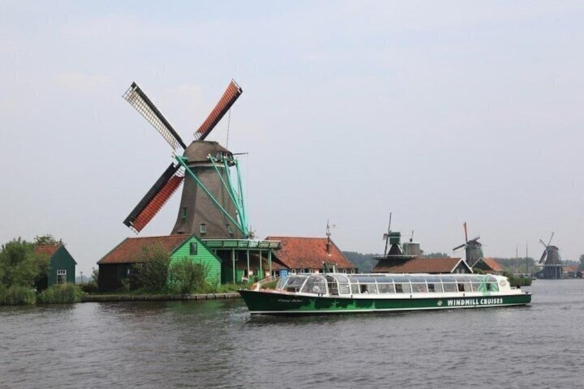 A green boat named 'Windmill Cruises' on water with a traditional windmill in the background. 2