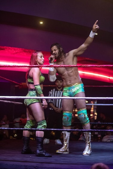 A wrestling ring with two wrestlers, one in green and the other in gold, and a referee in the background. 2