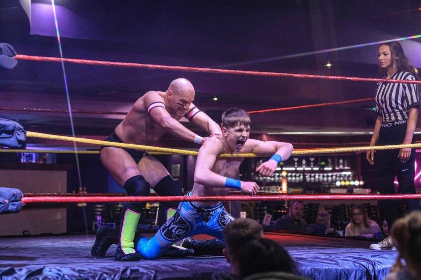 A wrestling match in a ring with a referee and an audience. 3