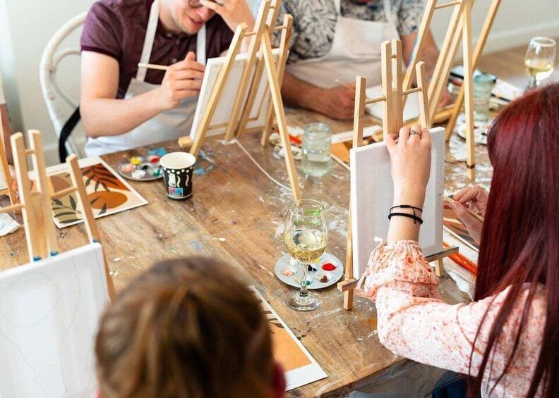 People painting on easels at a table with paint palettes and brushes. 5