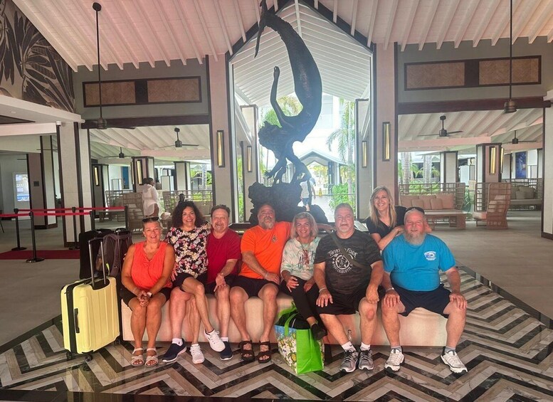 A group of people sitting on a bench in a covered outdoor area with a large sculpture in the background. 5