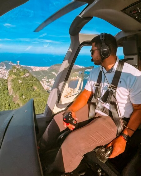 A person in a helicopter cockpit with a view of a city and a hill with a monument. 1
