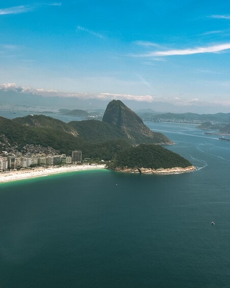 A coastal cityscape with a prominent mountain, a beach, and a bridge in the distance. 4