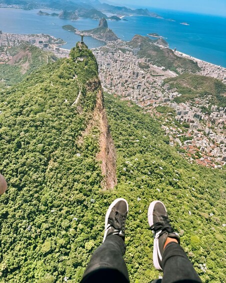 A person sitting on a mountain with a city and ocean in the background. 2