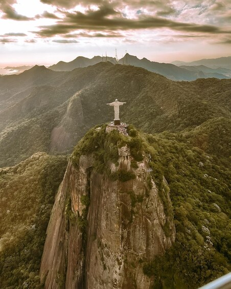 A large statue on a mountain peak with surrounding lush greenery and distant mountains. 5