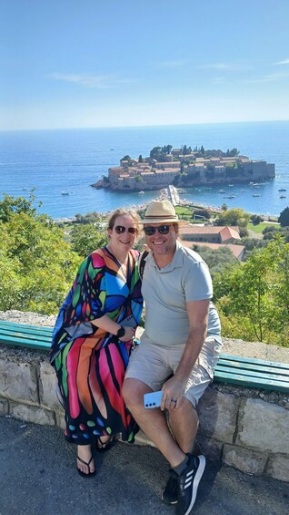 Two people sitting on a ledge overlooking a coastal town with a historic fort. 2