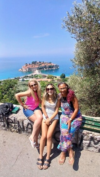 Three people sitting on a stone ledge overlooking a coastal town with a historic building. 1