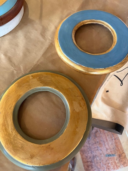 Two circular objects with a central hole, one painted blue and the other gold, placed on a table. 2