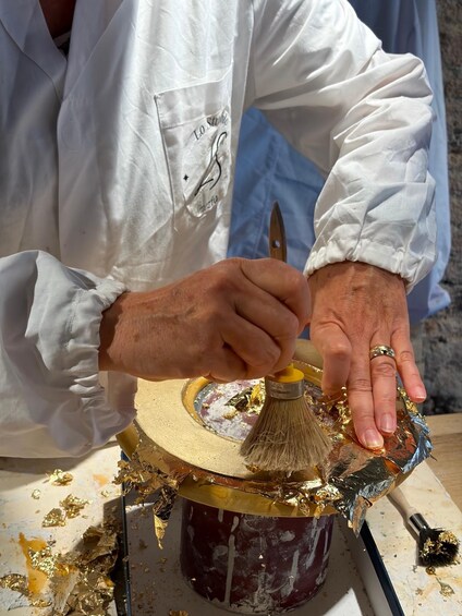 A person painting a wooden surface with gold leaf flakes. 5