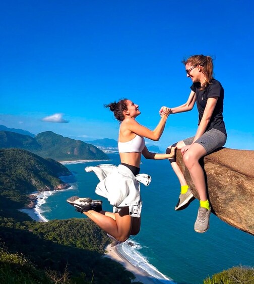 Two people jumping off a cliff with a coastal landscape in the background. 1