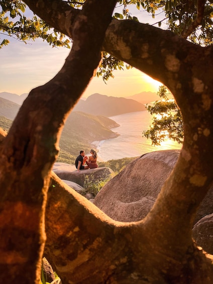 A couple sitting on a rock overlooking a coastal landscape with mountains in the background. 3