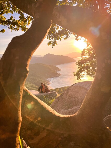 A couple sitting on a rock overlooking a coastal landscape during sunset. 2