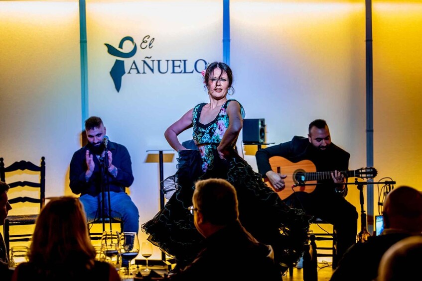 A woman in a black dress performing on stage with a band, in front of a sign that reads 'El NÃUELLO'. 1