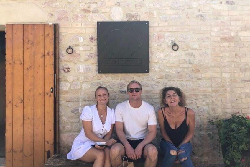 Three people sitting on a bench against a stone wall with a plaque and a wooden door. 2