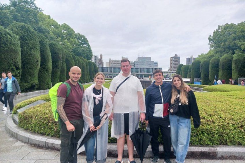 A group of people standing in a park with neatly trimmed hedges and a cityscape in the background. 2