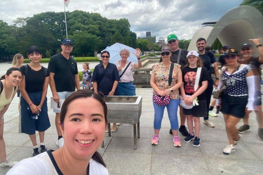 A group of people standing in a park with a fountain and trees in the background. 5