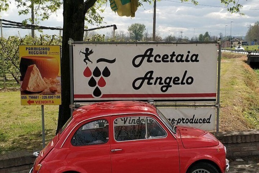 A vintage red car parked next to a sign for Acetaiia Angelo. 4