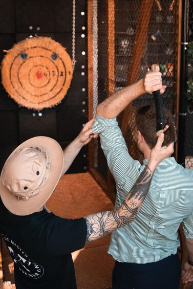 A person holding a bat, another person wearing a hat, and a target on the wall. 2