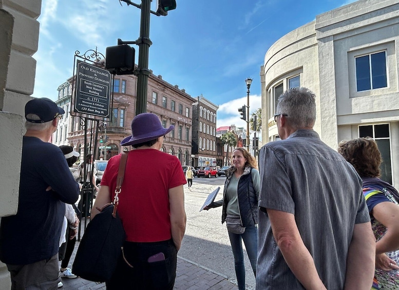 A group of people standing on a city street, a traffic light, and historic buildings in the background. 1