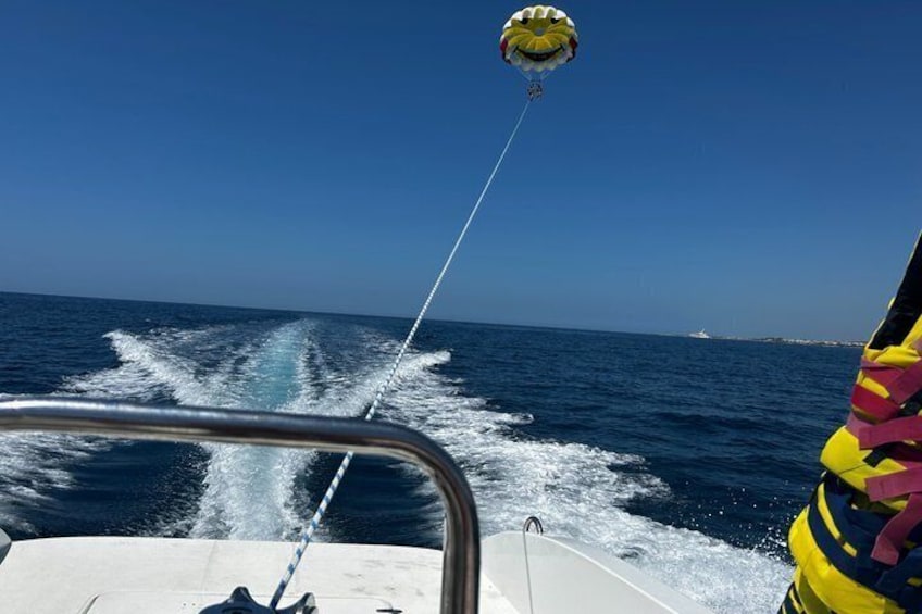 A parasail with a person in a yellow life jacket, a boat creating a wake, and a clear blue sky. 2