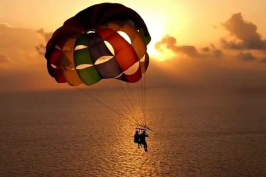A person skydiving with a colorful parachute over a body of water during sunset. 1