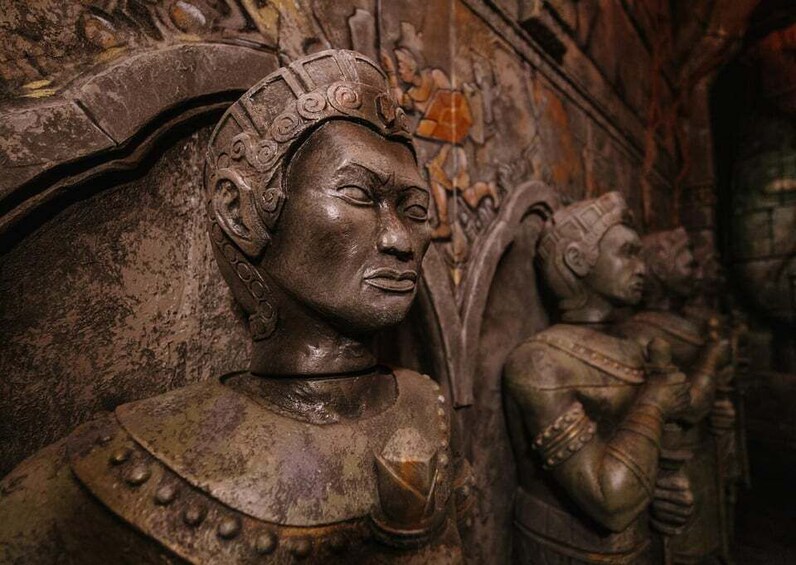 A detailed sculpture of a figure with ornate headgear and a shield, set against a textured wall. 4