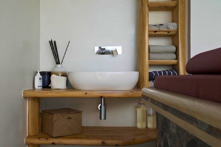 A modern bathroom with a white vessel sink, wooden shelves, a wooden ladder, and a red bath mat. 3