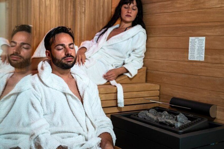 People in white robes in a sauna with wooden walls and a visible menu. 1