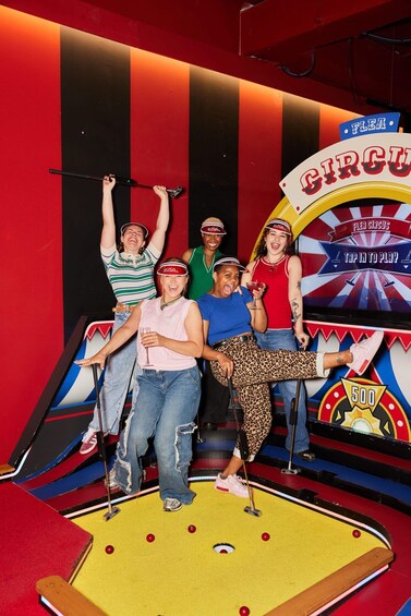 A group of people at a flea circus game with a dartboard and a sign that says 'FLEA CIRCUS'. 5