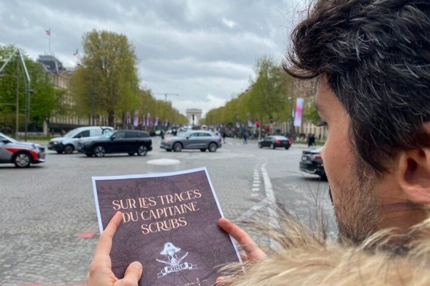 A person holding a book titled 'SUR LES TRACES DU CAPITAINE SCRUBS' with a city street in the background. 1