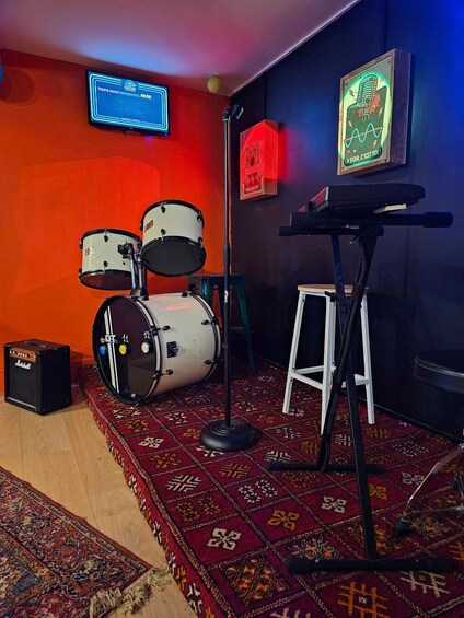 A drum set, a microphone stand, a small amplifier, and a patterned carpet in a room with orange walls. 5
