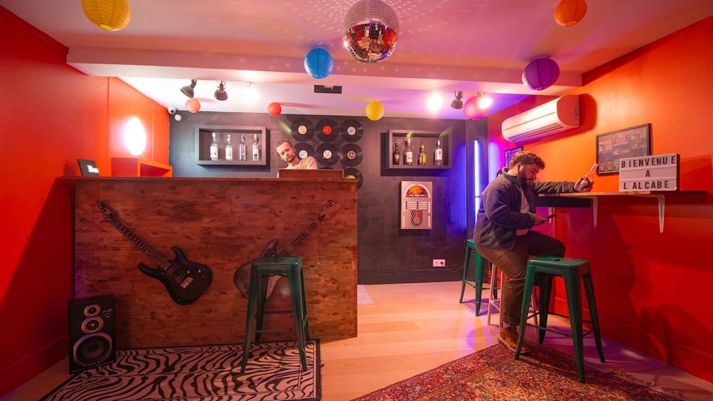 A room with a wooden partition, two guitars, a disco ball, and a DJ booth. 1