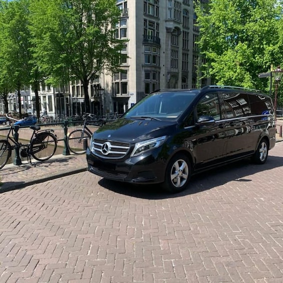 A black Mercedes-Benz van parked on a brick pavement with trees and a building in the background. 3