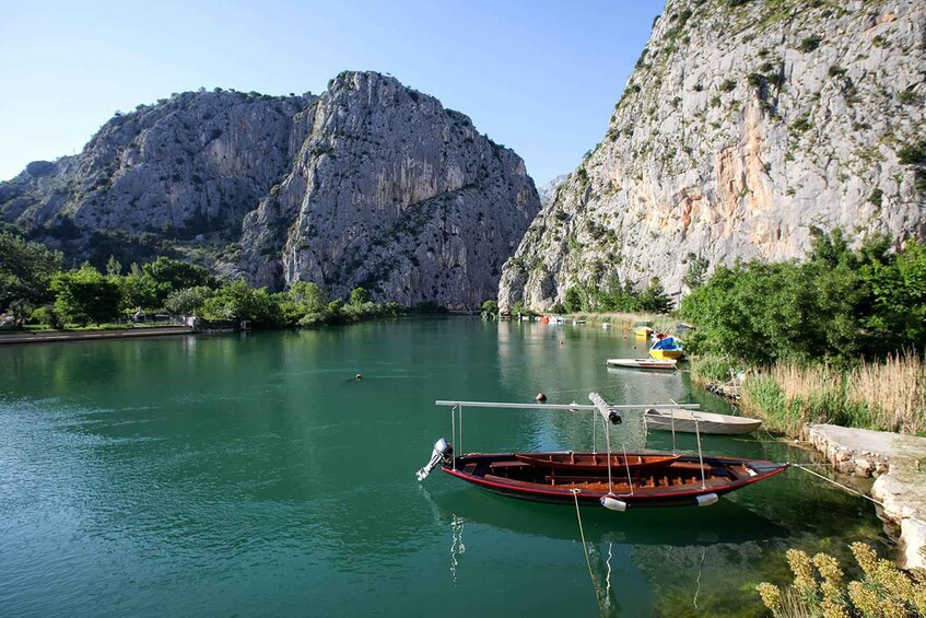 A calm river with boats, a rocky mountain, and lush greenery. 5