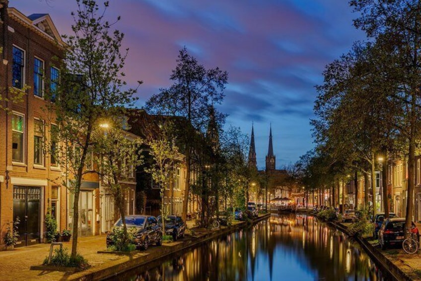A canal lined with trees and buildings, a church spire in the distance, and a sunset sky. 3