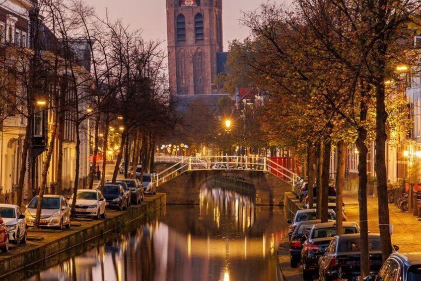A canal with a bridge, parked cars, trees, and a tower in the background. 2