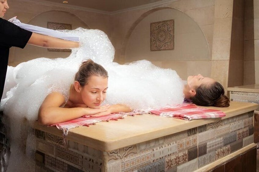 A person receiving a bubble bath treatment in a room with patterned tiles. 2