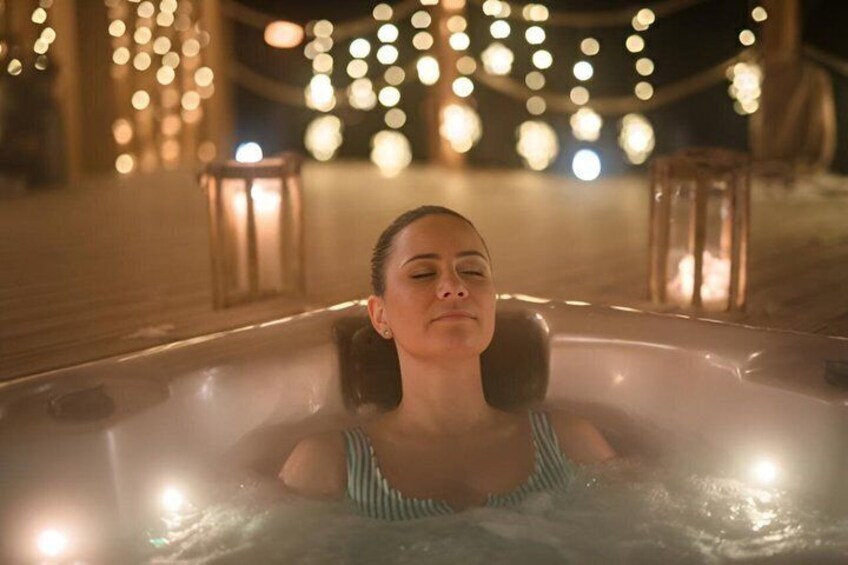 A person in a hot tub at night with string lights in the background. 4