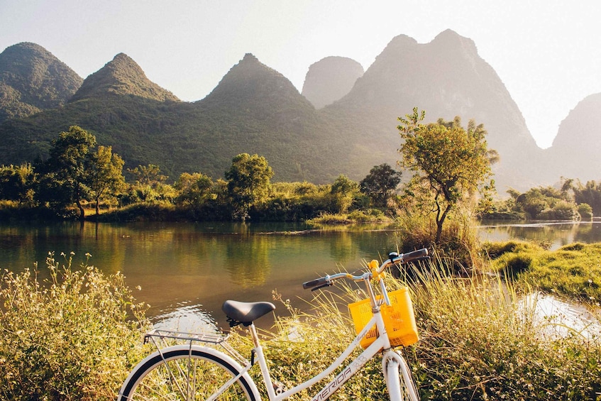 A bicycle parked by a river with mountains in the background. 3