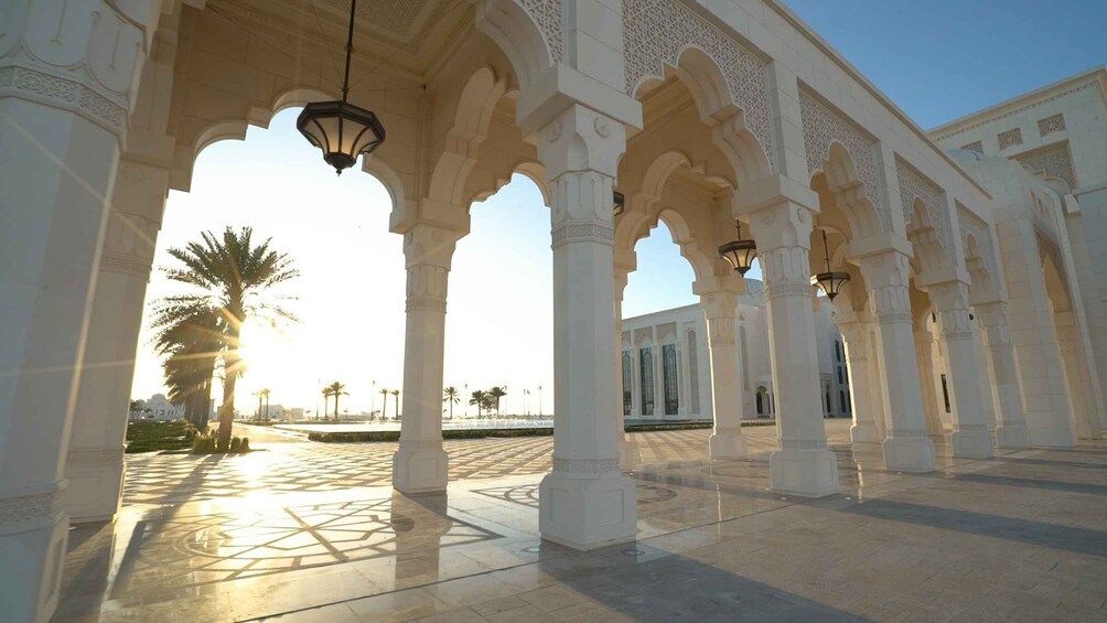 A courtyard with arches and columns, palm trees, and a building in the background. 3