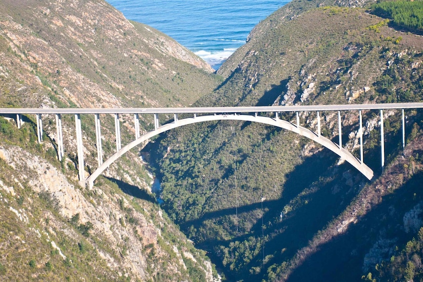 A bridge spanning a deep valley with steep cliffs and a body of water at the base. 3