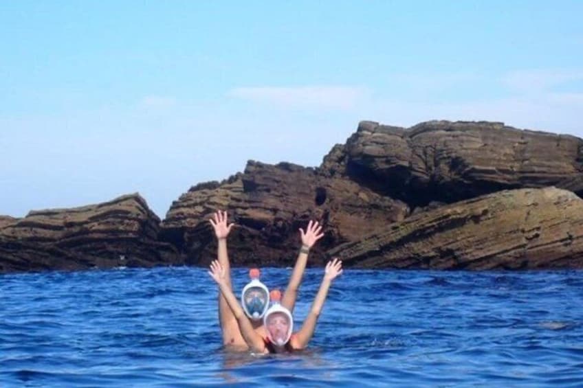 A person swimming in the ocean with rocky cliffs in the background. 2