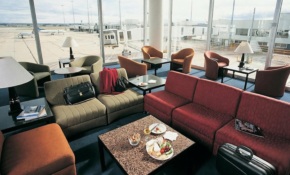 A modern airport lounge with leather couches, a coffee table with snacks, and a view of the airport tarmac. 2