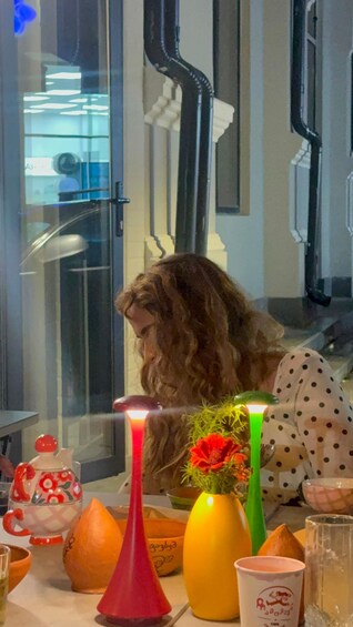 A person sitting at a table with various items including a red vase, a yellow vase, and a glass. 3
