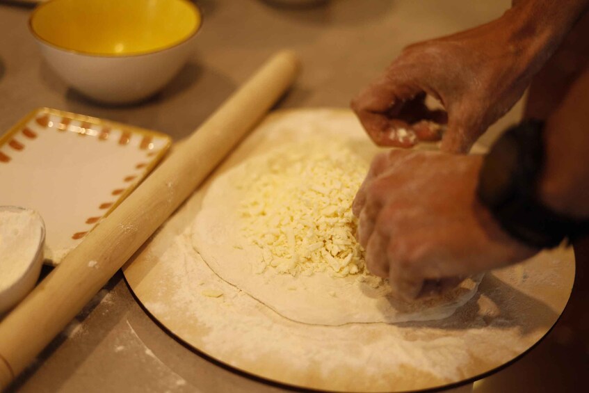 A person rolling out dough on a kitchen counter with a rolling pin and a bowl of flour nearby. 3